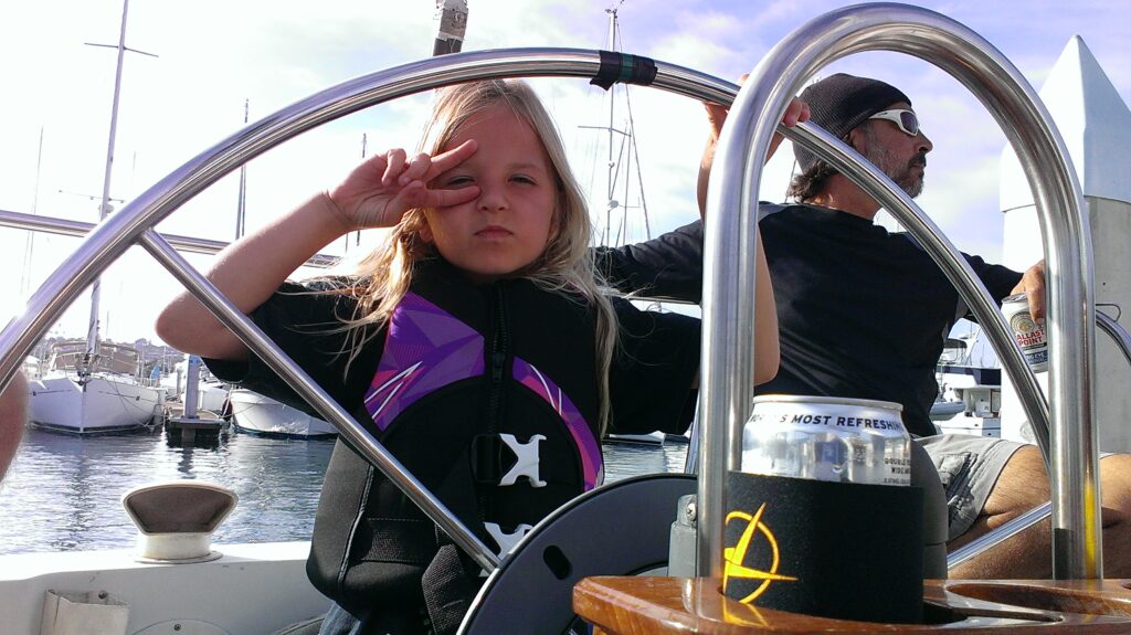 Child and man steering a sailboat at marina