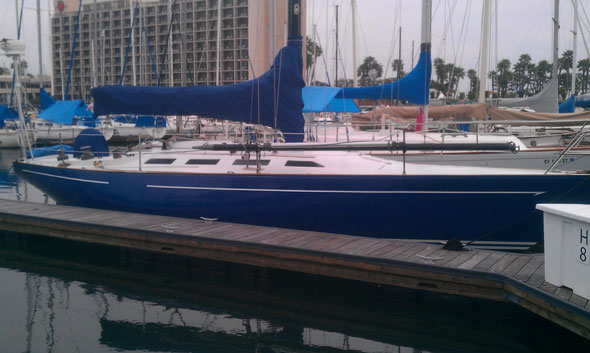 Blue sailboat docked at marina near tall buildings
